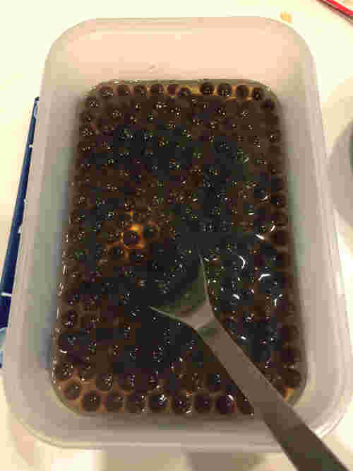 タッパーに入っている黒いタピオカをスプーンですくっている様子