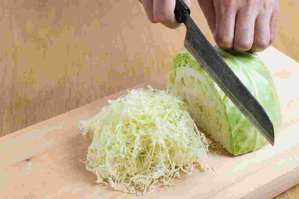 まな板の上で半玉キャベツに手を添えて包丁でカットしようとしている