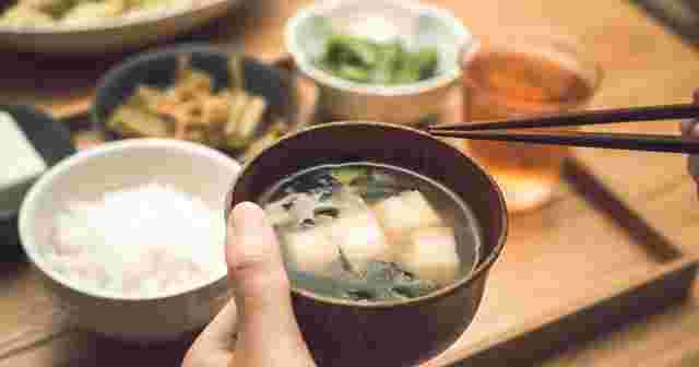味噌汁を手に持ち箸で食べようとしている画像
