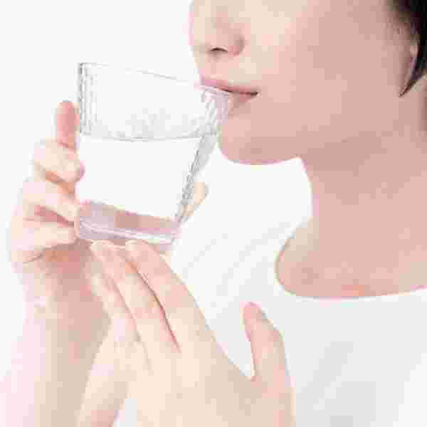グラスに注いだ水を飲む女性