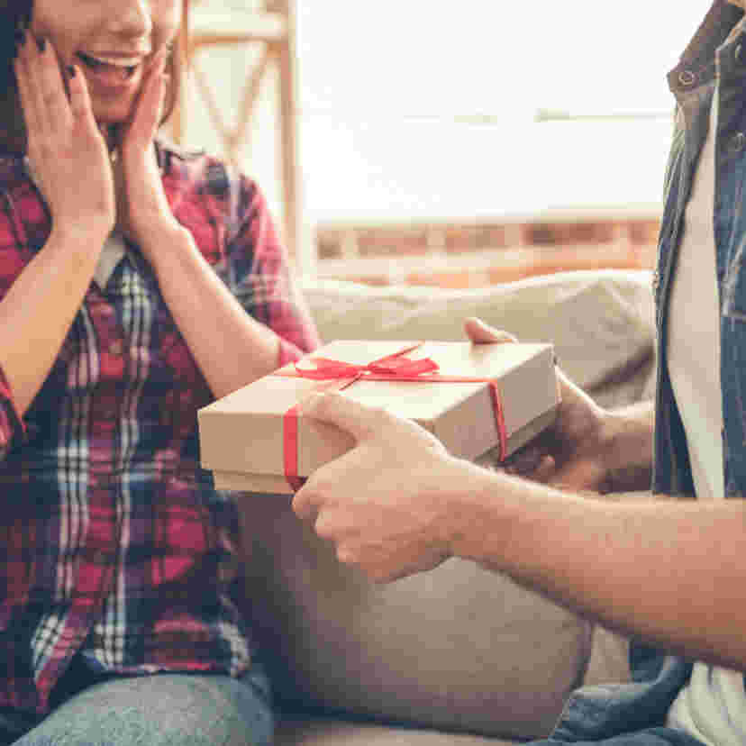 茶色い箱に赤いリボンが付いたギフトを手渡ししている