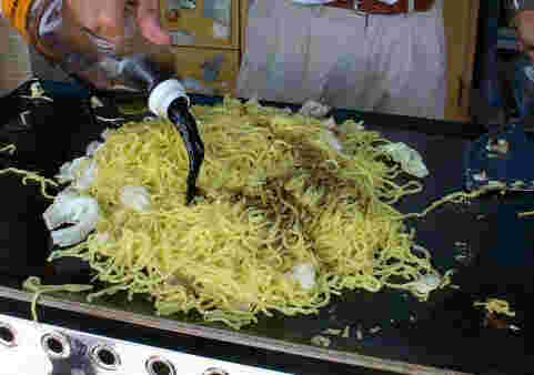屋台の焼きそば麺にソースをかけている