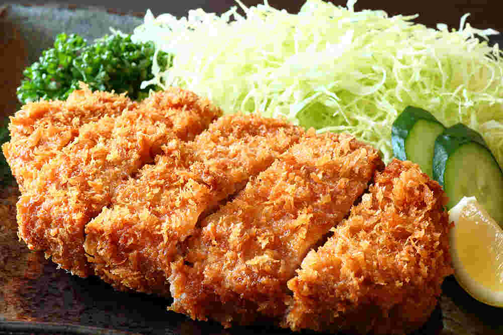 とんかつと同じ皿にキャベツ、レモン、キュウリ、パセリが乗っている様子