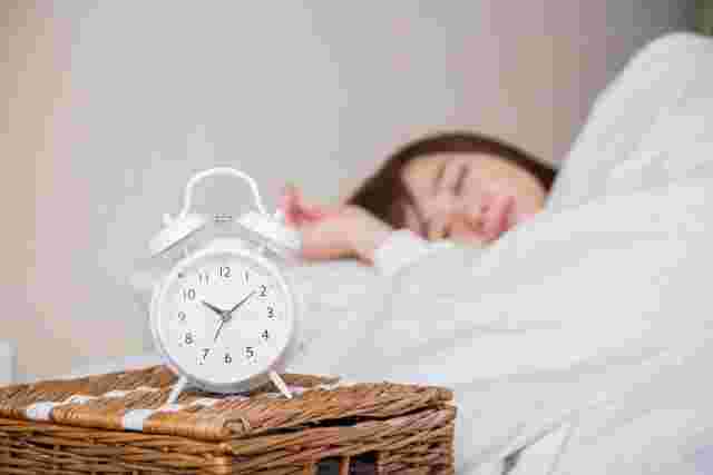 寝ている女性の手前に目覚まし時計が置かれている