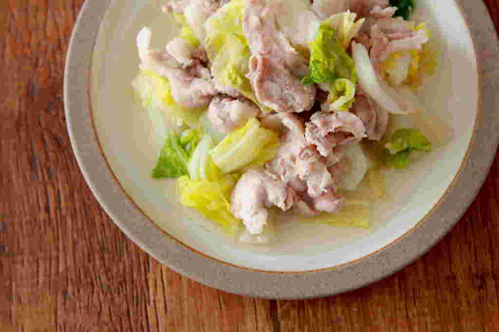 木製のテーブルにグレーと白の皿に盛られた白菜と豚肉のおかず