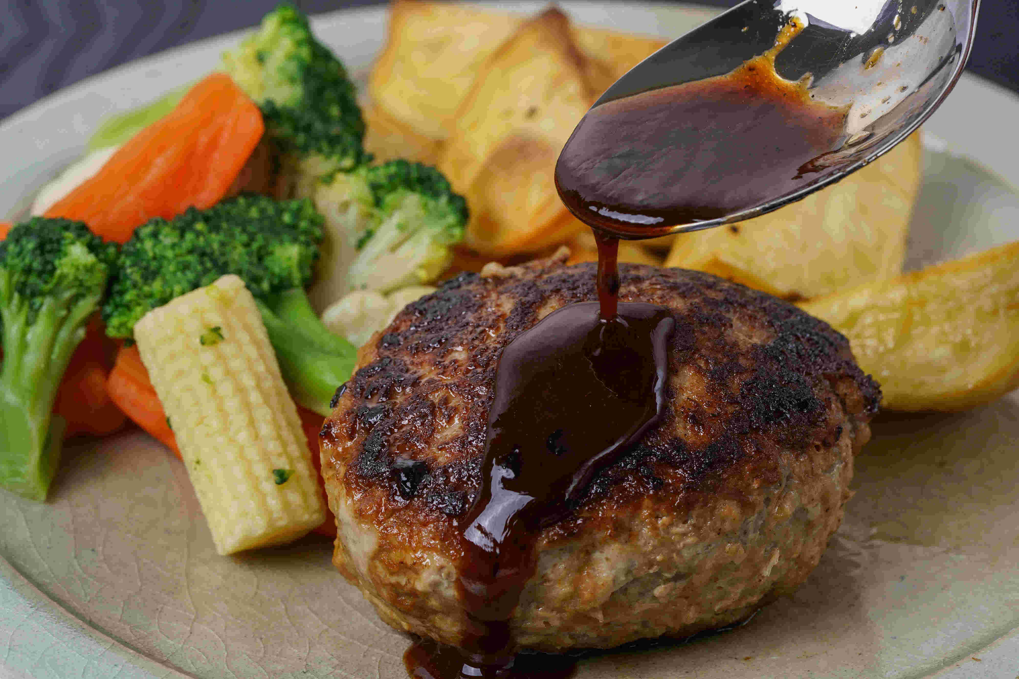 ハンバーグや付け合わせ野菜、ポテトを皿に盛り付け、ハンバーグソースをかける