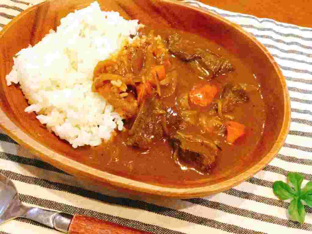 木の丸い器に白ご飯少量、一口大の肉、ニンジン、薄い玉ねぎがたっぷり入ったカレールーが盛り付けられている