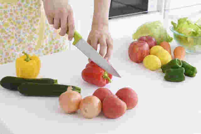 パプリカを切る女性と周りに置いてある野菜や果物