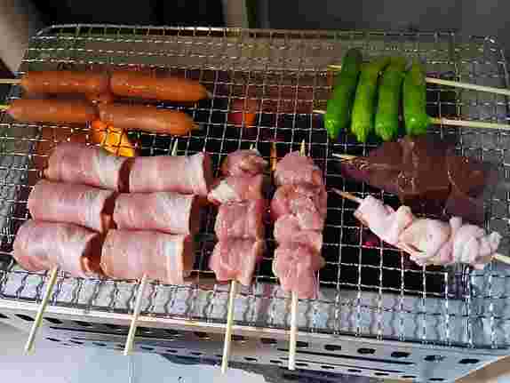 網焼きの上に置かれた焼き鳥とベーコン巻きとシシトウ