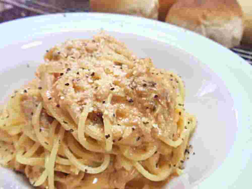 白い丸い皿にパスタと玉ねぎと少し茶色のクリームがかかり盛られている