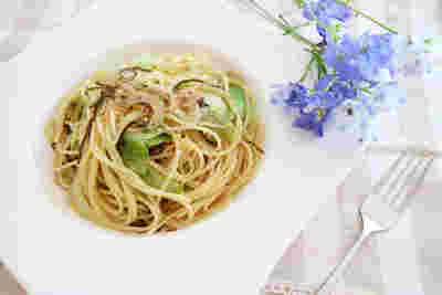 白い四角い皿の上にパスタ、レタスなどが盛り付けられていて、横に青い綺麗な花とフォークが置かれている