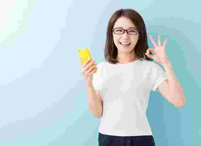 スマホを片手にOKサインをだす笑顔の女性