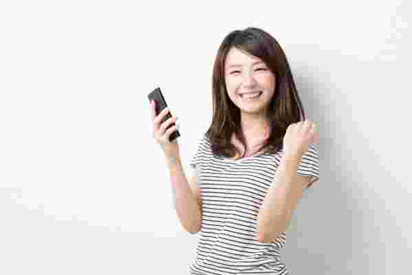 スマホを見ながらがらガッツポーズをする笑顔の女性