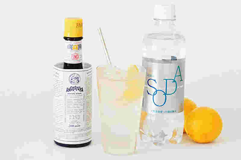 丸いオレンジ、ソーダ―と記載された小さめのペットボトル、コップにストローとカットされたオレンジと飲み物、小さいボトルビンが置かれている