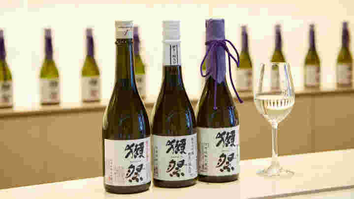 獺祭というお酒が3本並び、その横に透明なワイングラスが置いてある様子