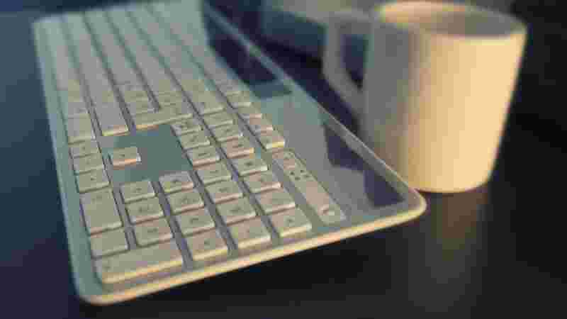 パソコンのキーボードと白のコーヒーカップが並んでいる様子
