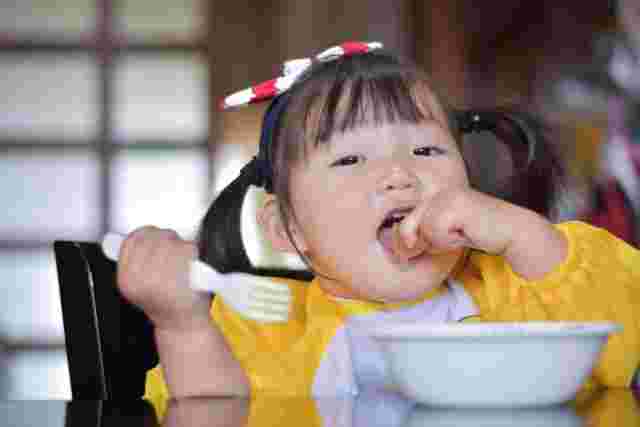 フォークを持って手づかみで食事する赤ちゃん