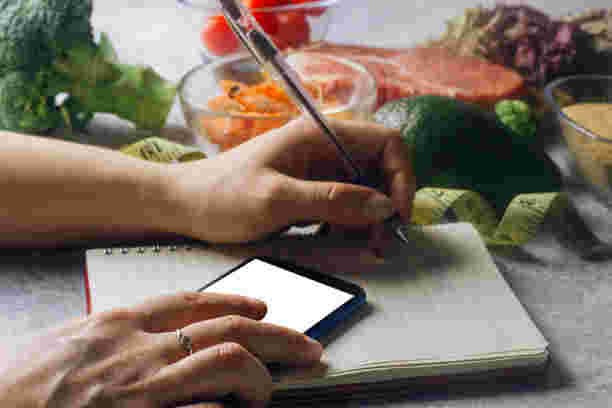 まわりに食材が並べられている中でスマホ片手にノートにメモを取る