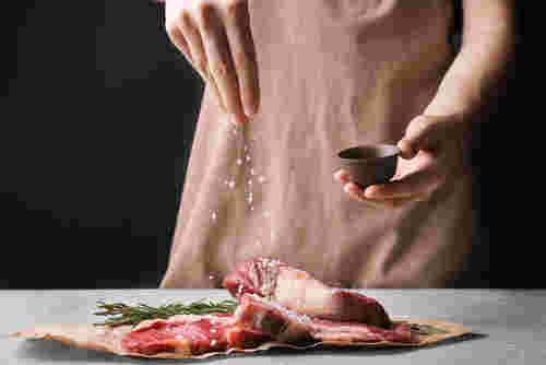 肉に岩塩をふりかける女性