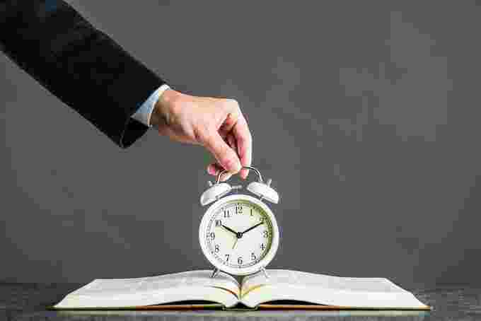 スーツを着た男性が開いた本の上に時計を置いている様子