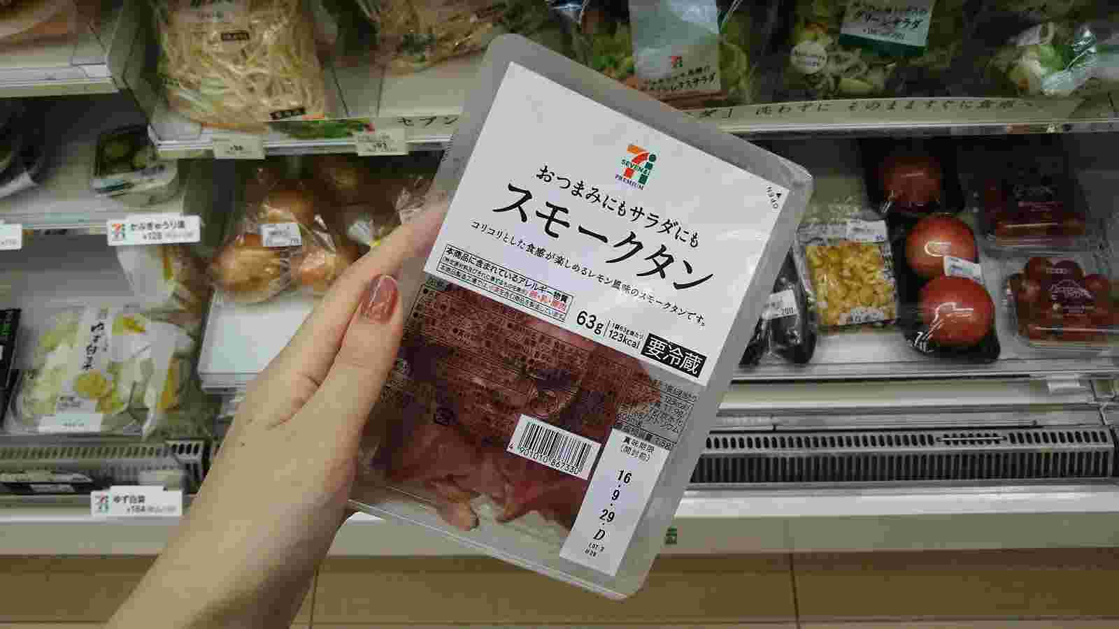 冷蔵の陳列棚の前で左手でスモークタンと記載された真空パックを持っている