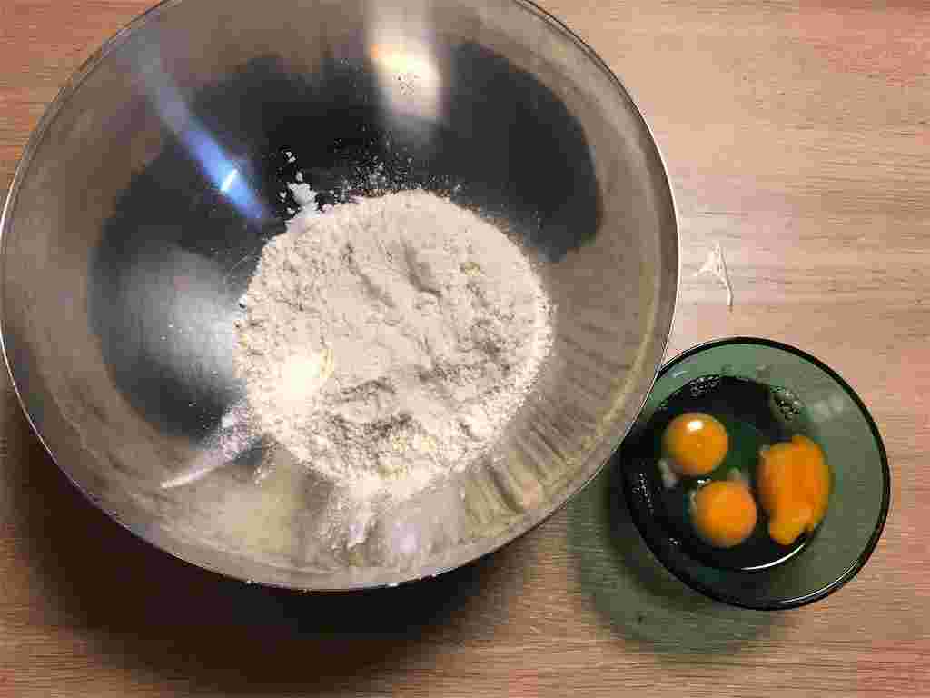 木製のテーブルにボウルに入った粉と割ったたまご