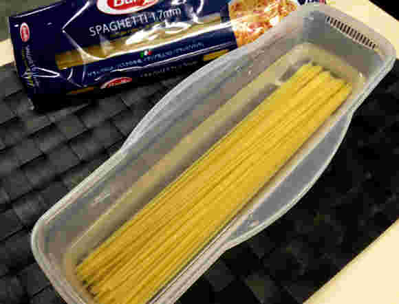 黒いランチョンマットの上に透明な箱にパスタが浸かっている
