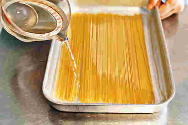 バットに入れた乾麺パスタに水をかける