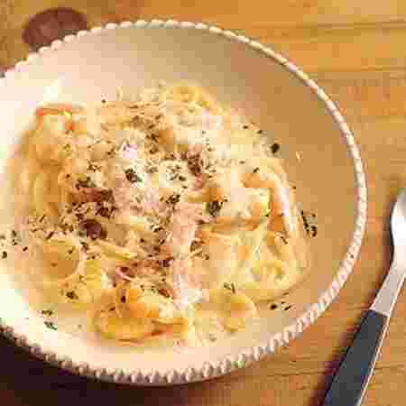 青いフォークと丸いお皿に入ったクリームソースのパスタ