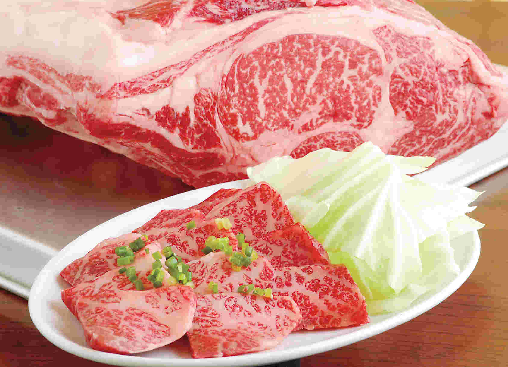 白いさしが入った霜降り肉の塊とスライスされ、隣にキャベツが添えてある霜降りの肉