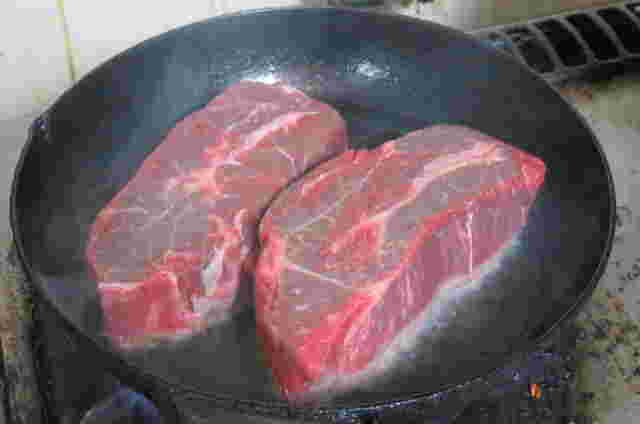 鉄板で焼かれる赤黒い2枚の大きな牛肉