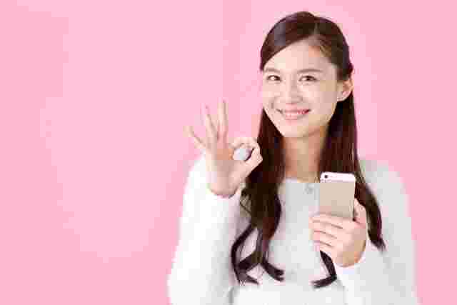スマホを片手にOKマークをする女性