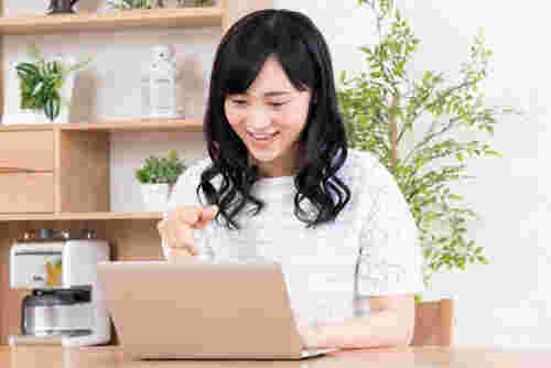パソコンを開きながら指差しをしている笑顔の女性