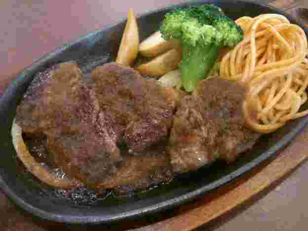 黒い鉄板の上にジューシーな肉汁を出す、ソースのかかったステーキが盛られている