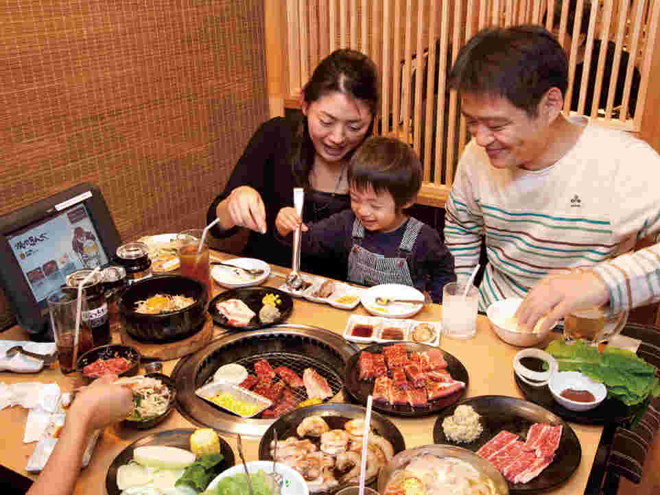 夫婦らしき2人と間に挟まれた幼児が楽しそうにテーブルの網で焼かれた焼肉を食している