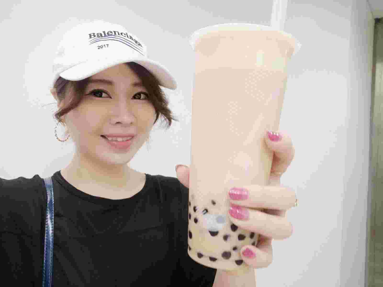 CoCo都可の若干茶色いタピオカドリングを手に持つ黒いシャツの白い帽子を被った女性
