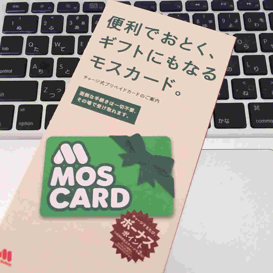 パソコンのキーボードの上にモスカードの絵がデザインされた茶色い封筒らしきものがある
