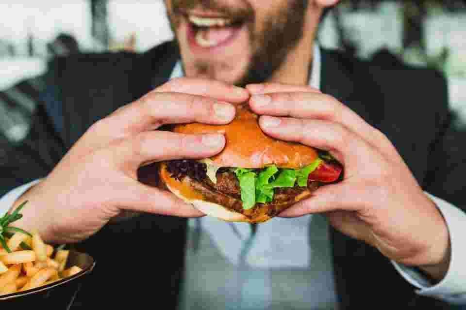 包み紙を外したハンバーガーを両手に持つ男性