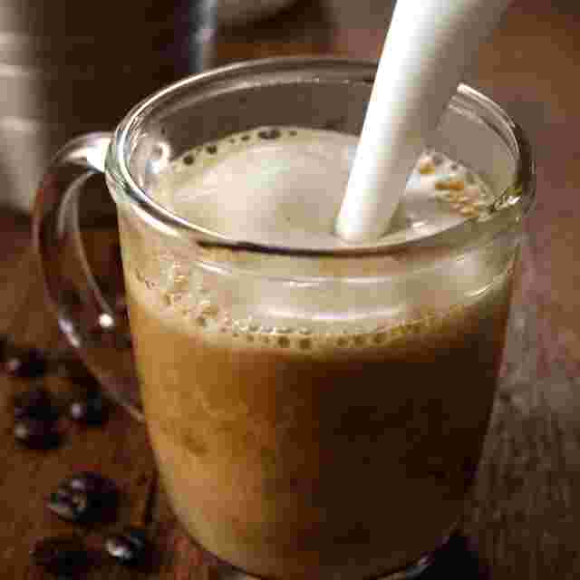 透明のカップに入ったコーヒーにミルクを注いでいるところ