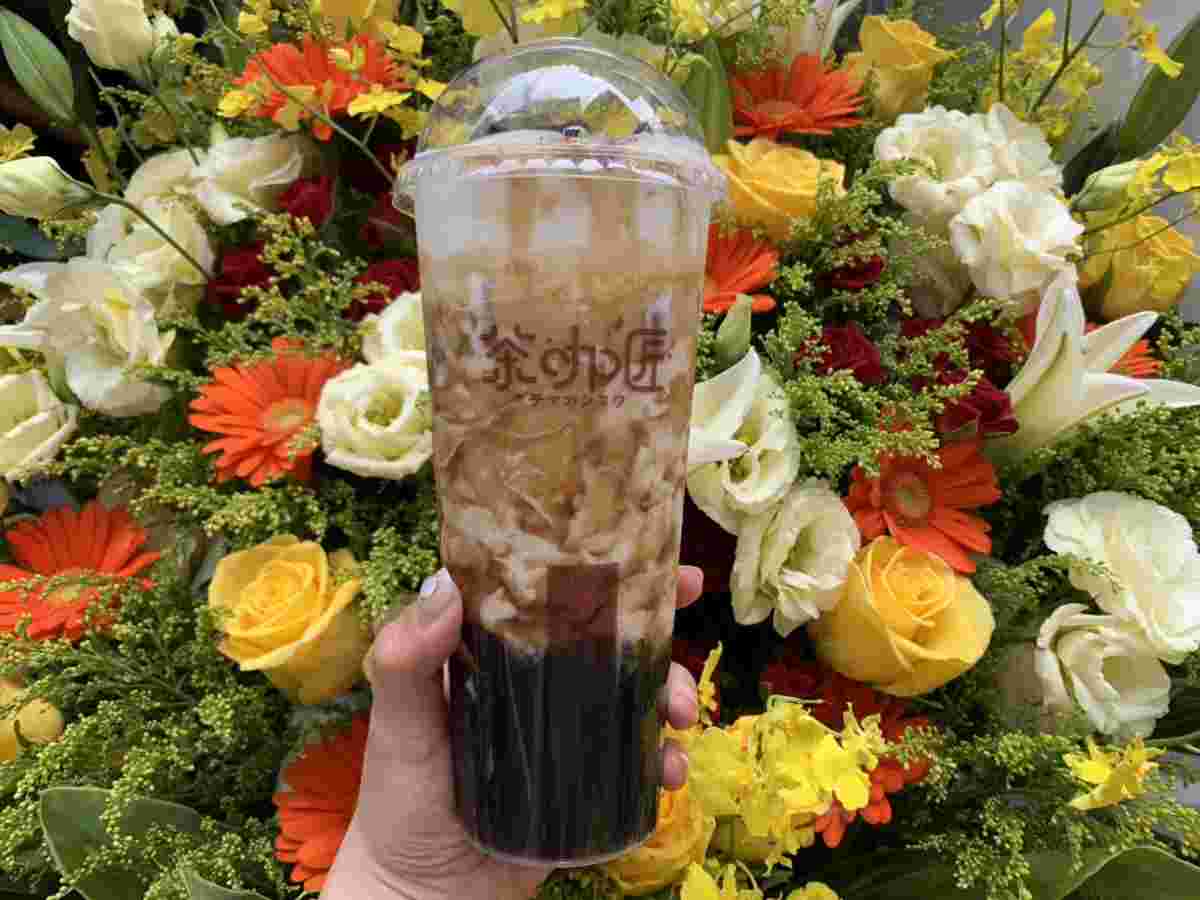 花束の前で片手にドリンクを持っているところ。