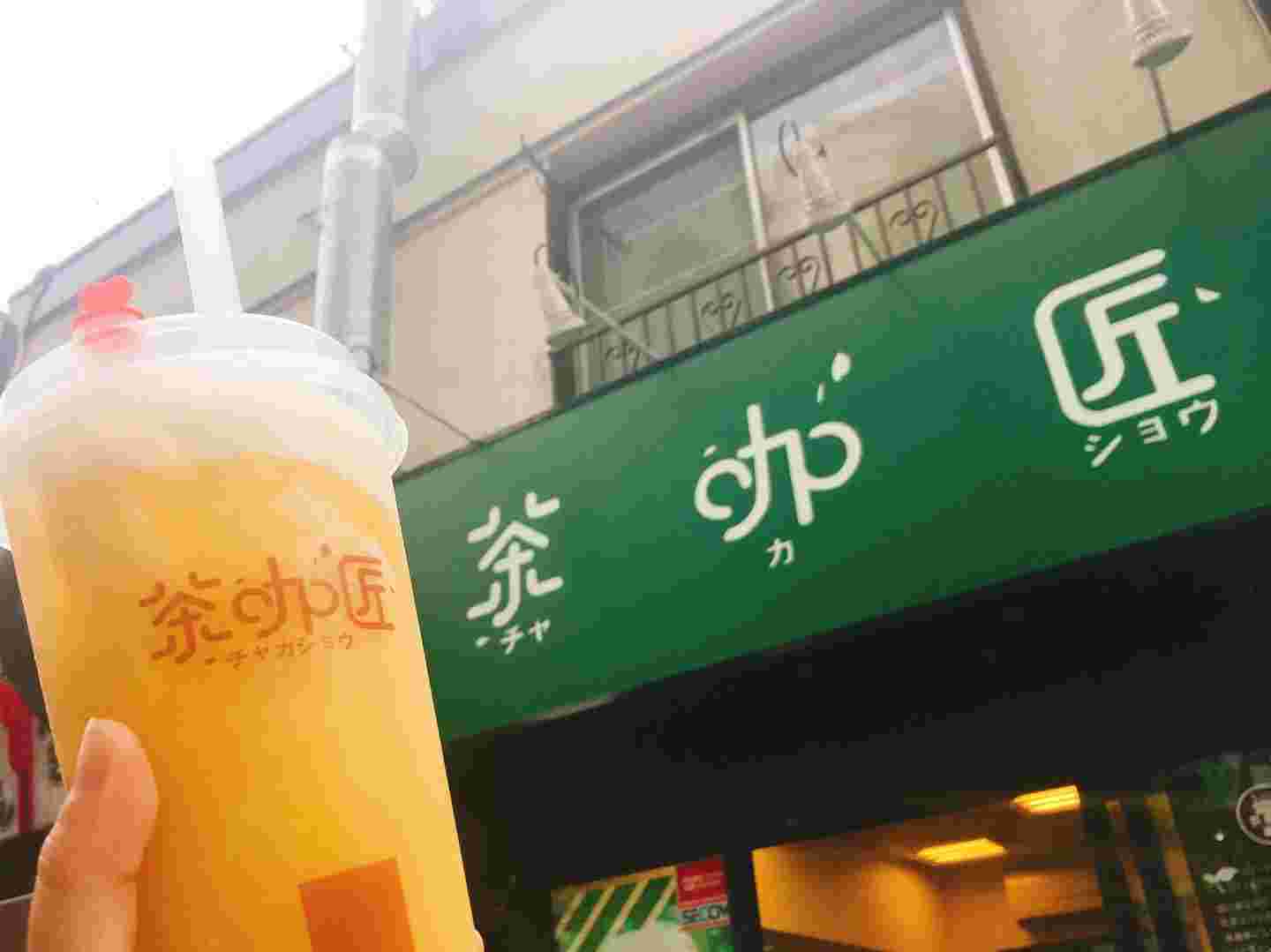 お店の前で片手での飲み物を持っている人の風景。