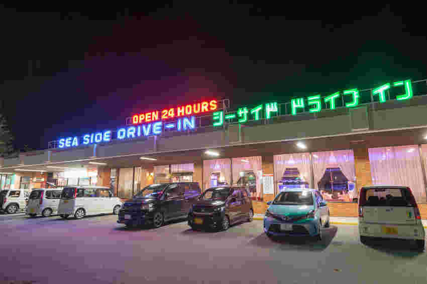 ネオンがきらめくお店と車が並べられて停めてある