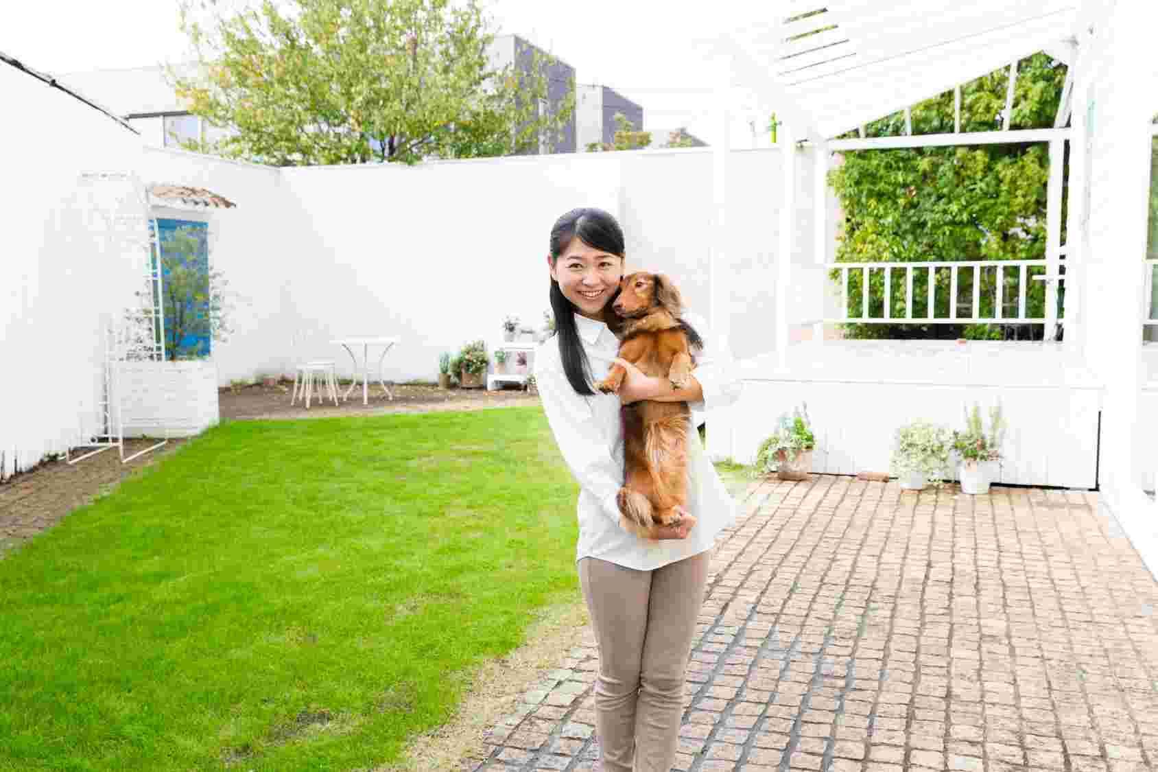屋外の庭で女性が犬を抱いている様子。