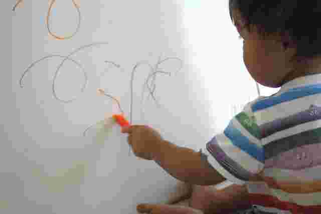白い壁にクレヨンで落書きをしている子供の様子