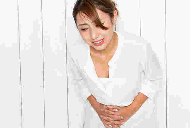 白い服を着た女性がお腹を抱えている様子。