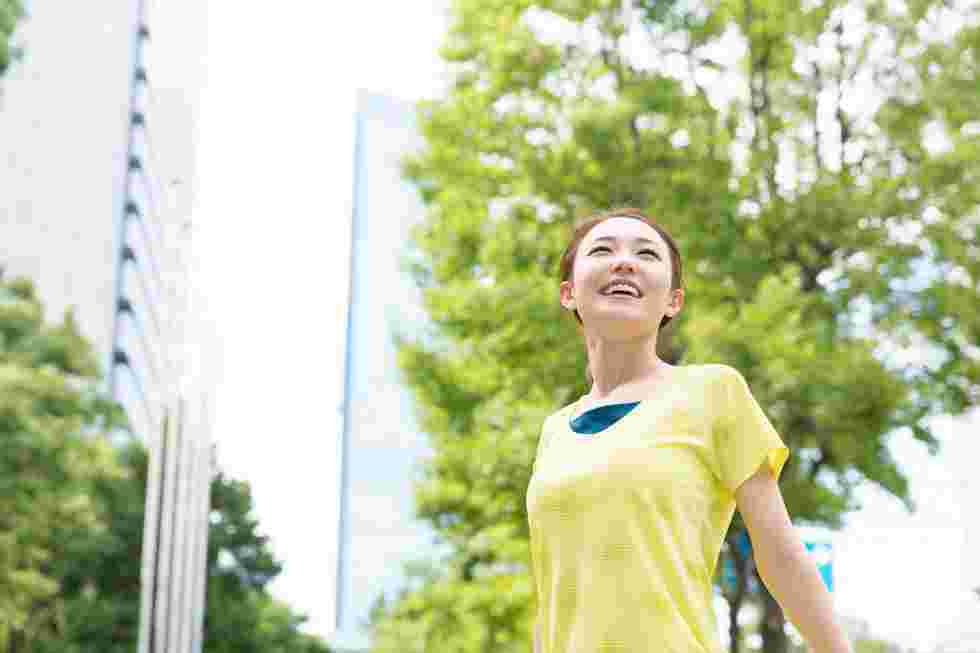 ビル街の緑の下で女性が立っている様子。