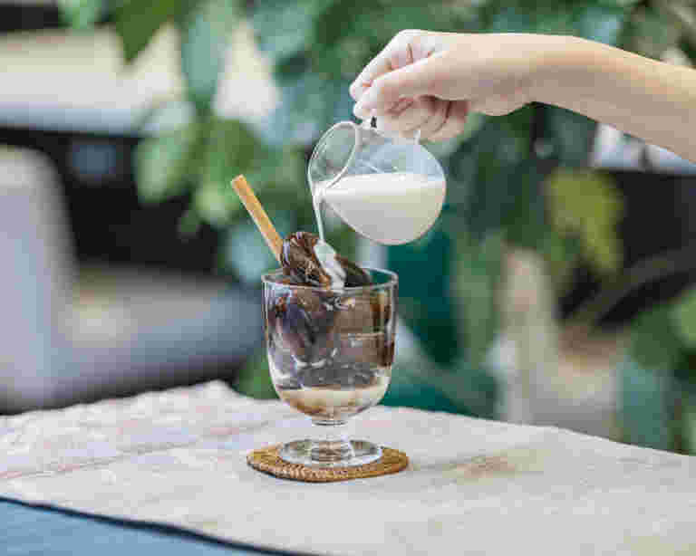 凍らせたコーヒーを入れたグラスにシナモンスティックを刺し、豆乳を注いでいる