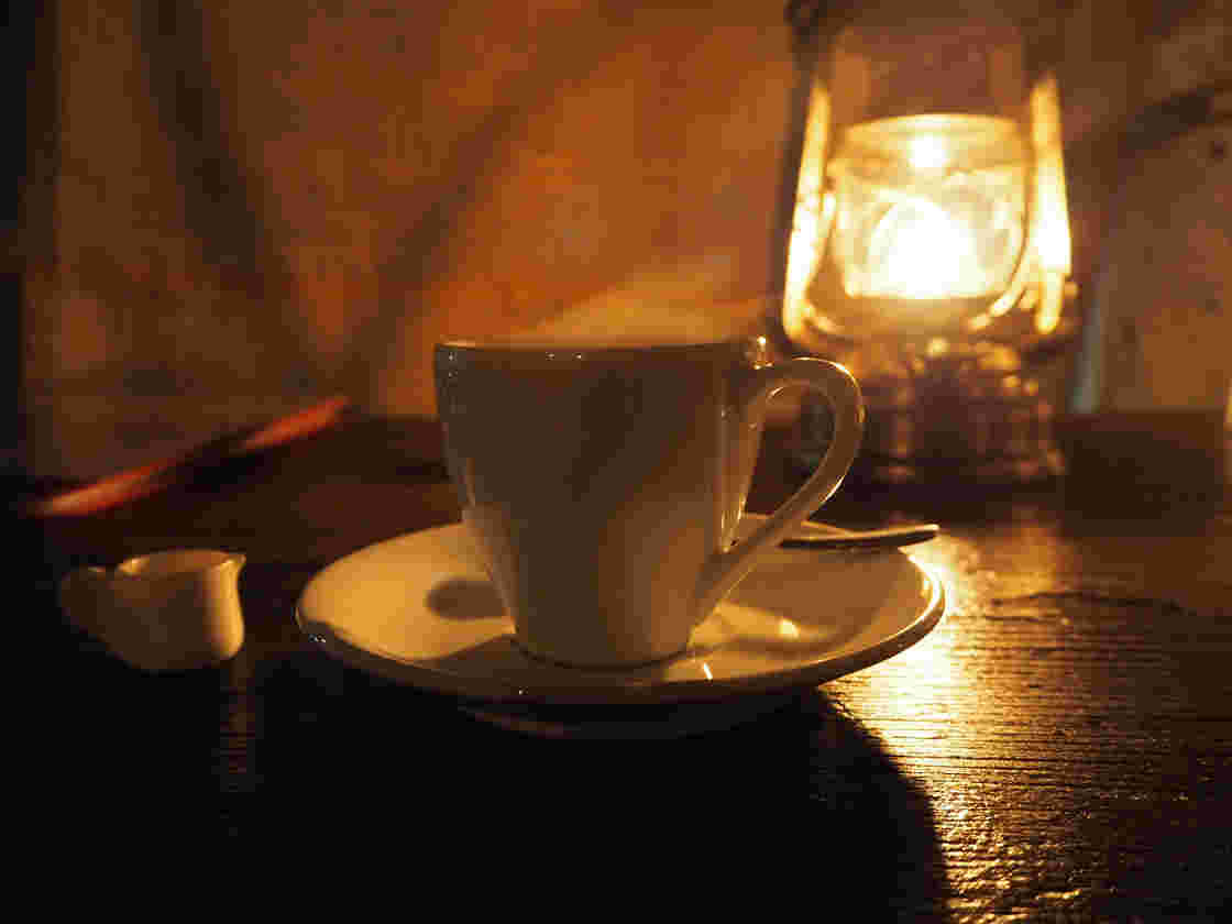 夜の暗がりにランプを置いてコーヒーカップを照らしている