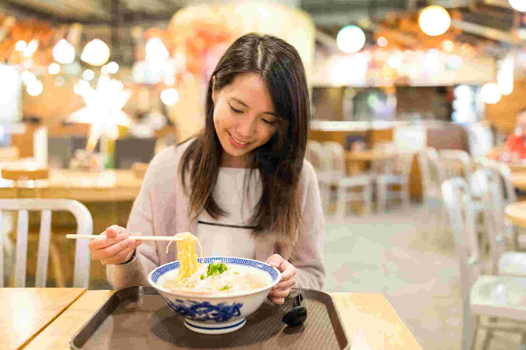 フードコートでラーメンをオーダーし、ラーメンをすくう女性