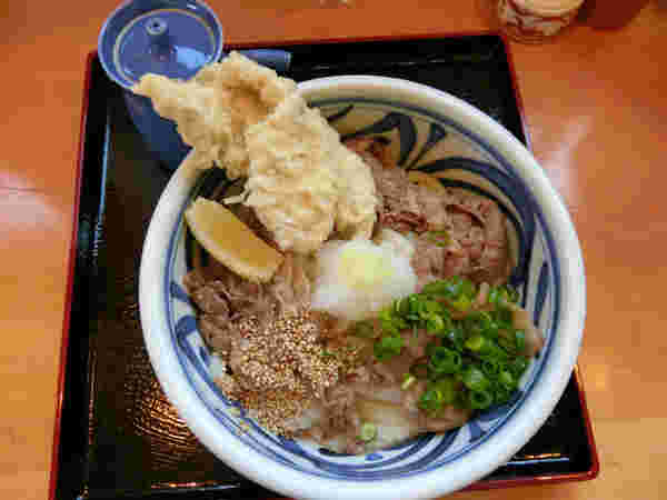 肉うどんに揚げ物がトッピングされている様子